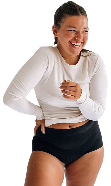 Smiling woman wearing a long-sleeve white shirt and black underwear stands against a plain white background.
