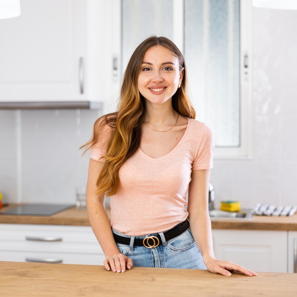 Portrait of woman in casual clothes posing near table at light kitchen