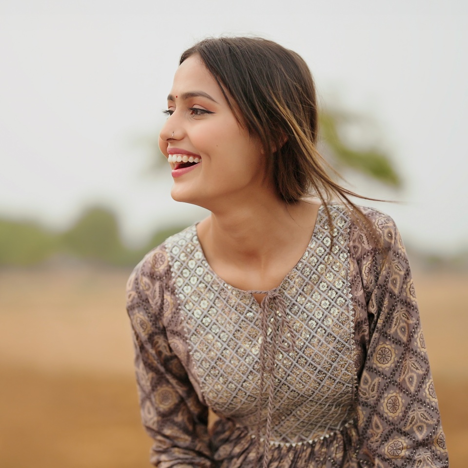 Indian young adult gen z farmer woman wear casual dress enjoying outdoor farmland. Asian happy smiling village teen age girl posing for cam outside ground