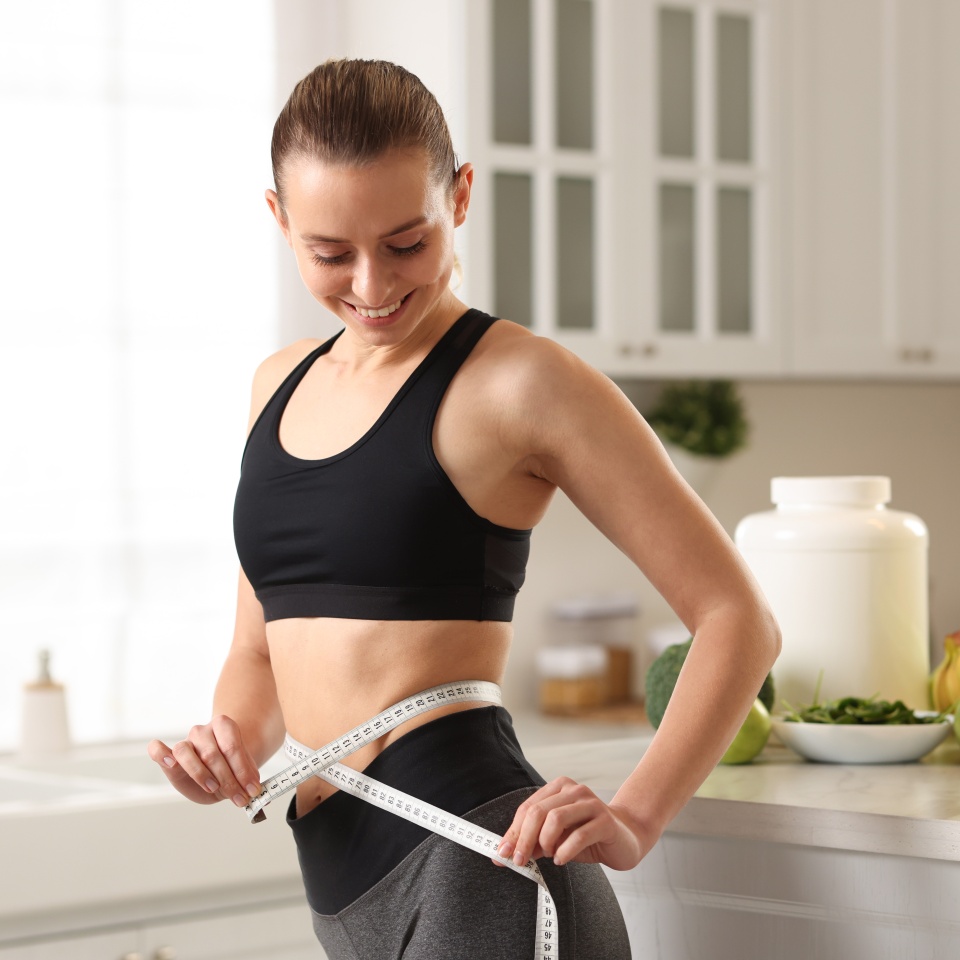Weight loss. Woman measuring waist with tape in kitchen