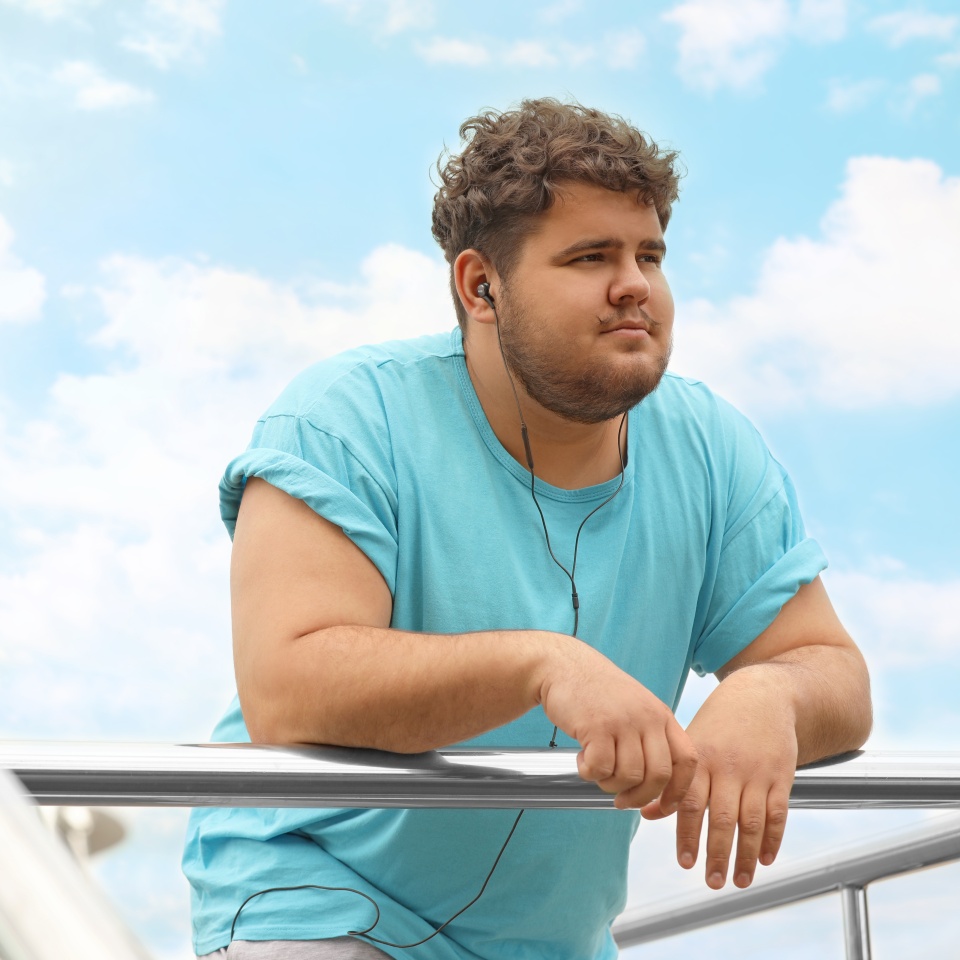 Young overweight man leaning on railing outdoors