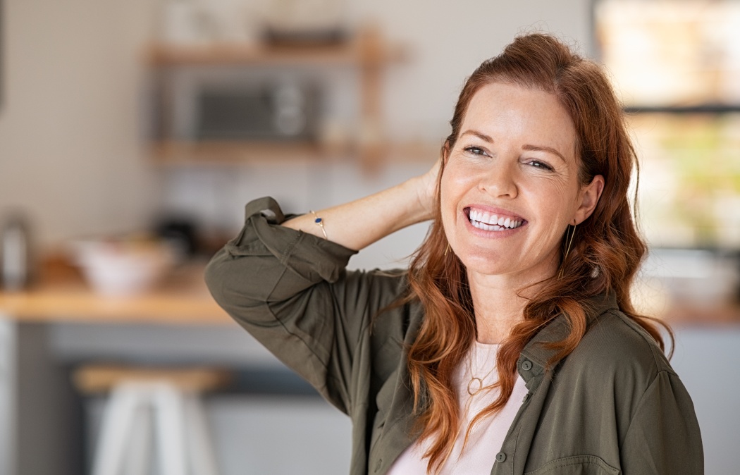 Portrait of beautiful mature woman at home. Successful middle aged woman smiling and looking away while touching hair. Mid redhead lady laughing and relaxing.