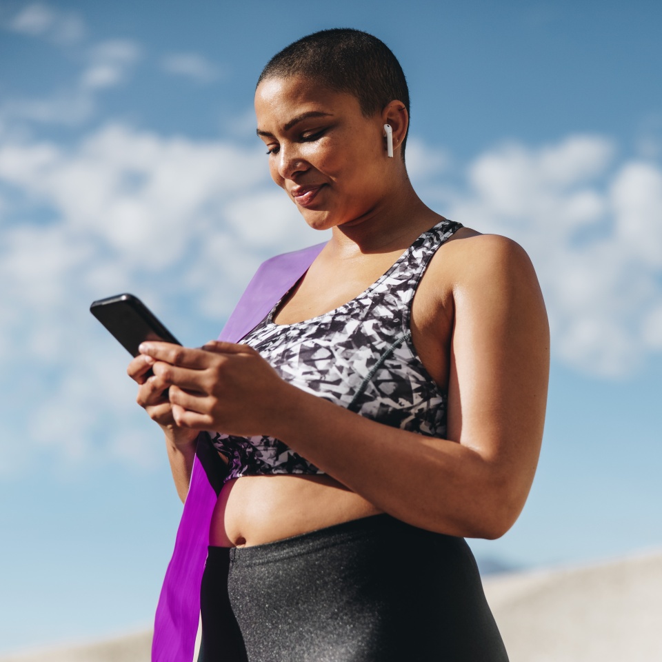 Female in sportswear using her smart phone after workout session. Healthy woman wearing wireless earphones taking a break from workout and checking her fitness progress on mobile phone.