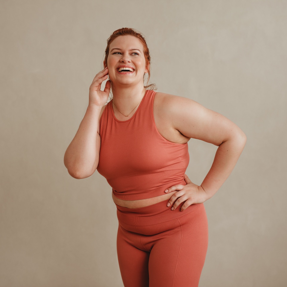 Confident woman in sportswear looking away and smiling. Healthy plus size female standing against a wall in gym.