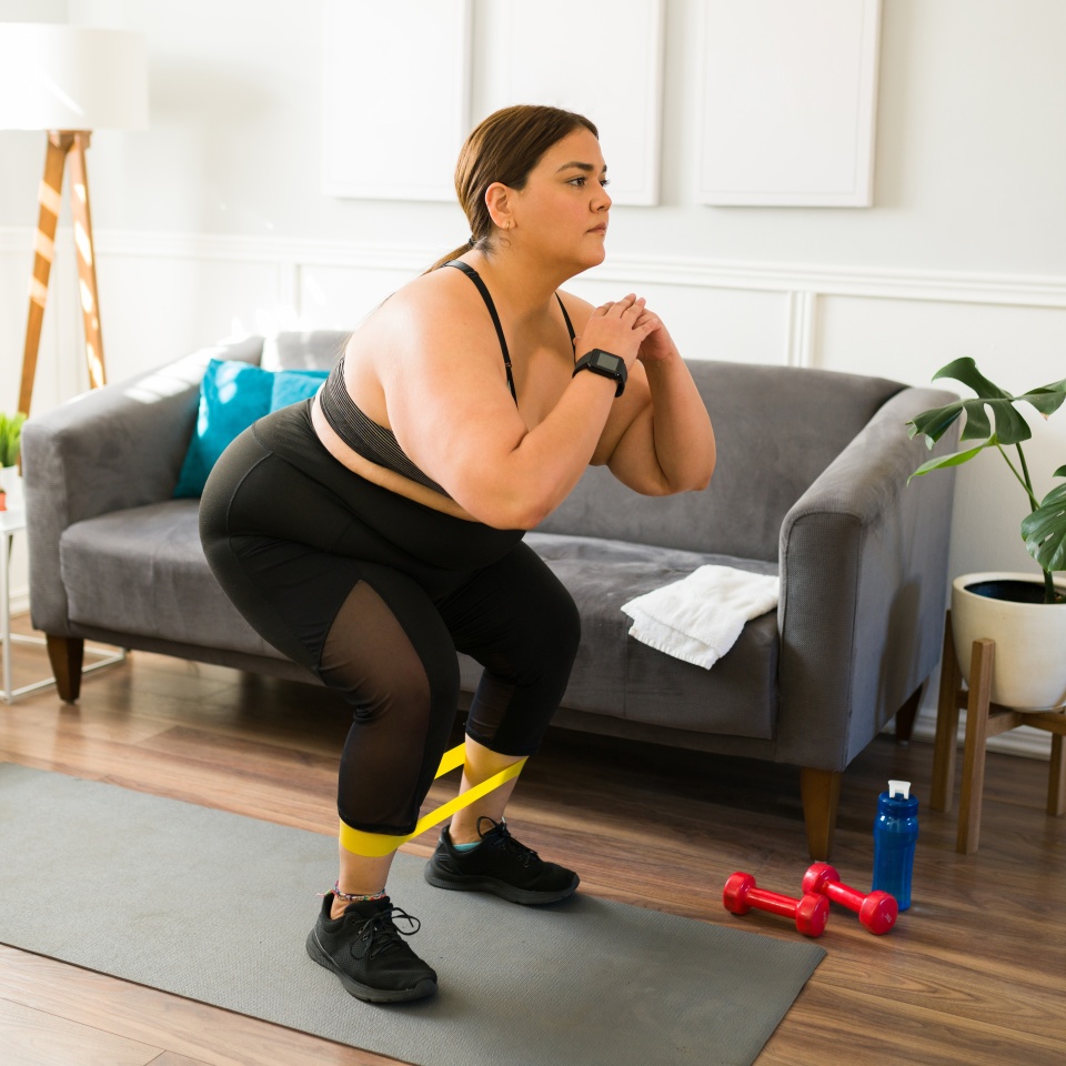 Focused fat young woman using a resistance band while exercising. Overweight woman doing a strong workout