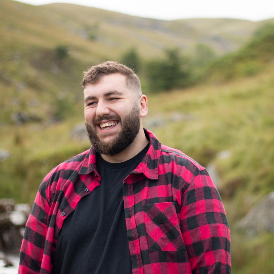 Plus size male with beard wearing a checked shirt while out on a travel adventure on a welsh mountain