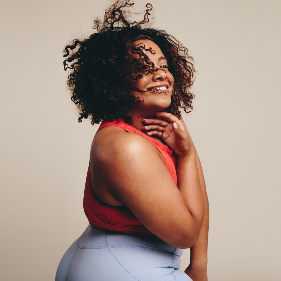 Fit woman in sportswear smiling at the camera in a studio. Woman having fun as she embraces her body and curvy physique, expressing self-assurance through dance movement and physical activity.