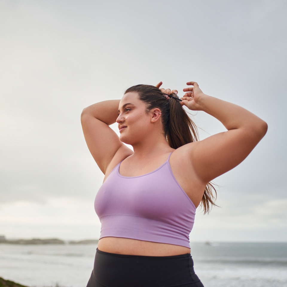Relaxed smiling woman looking away and correcting hair while walking at the sea