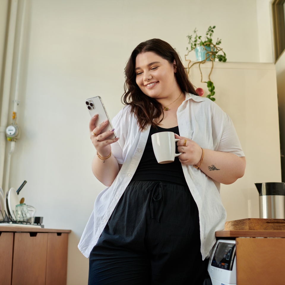 Bright morning at home with a plus size woman sipping coffee and checking her phone.