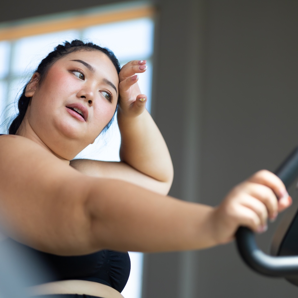 Tired fat asian woman on cycling. beautiful young chubby overweight woman wearing sporty fitness clothes doing exercise indoors at gym fitness sport club, body and health care