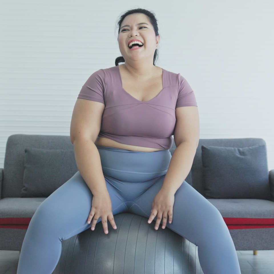 Happy Asian fat woman sitting on exercise fitness ball