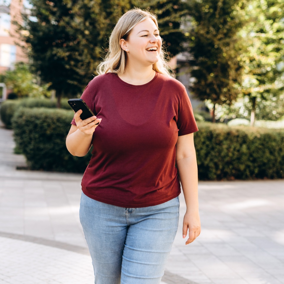 Portrait of positive plus size young Caucasian woman standing outdoors using mobile phone