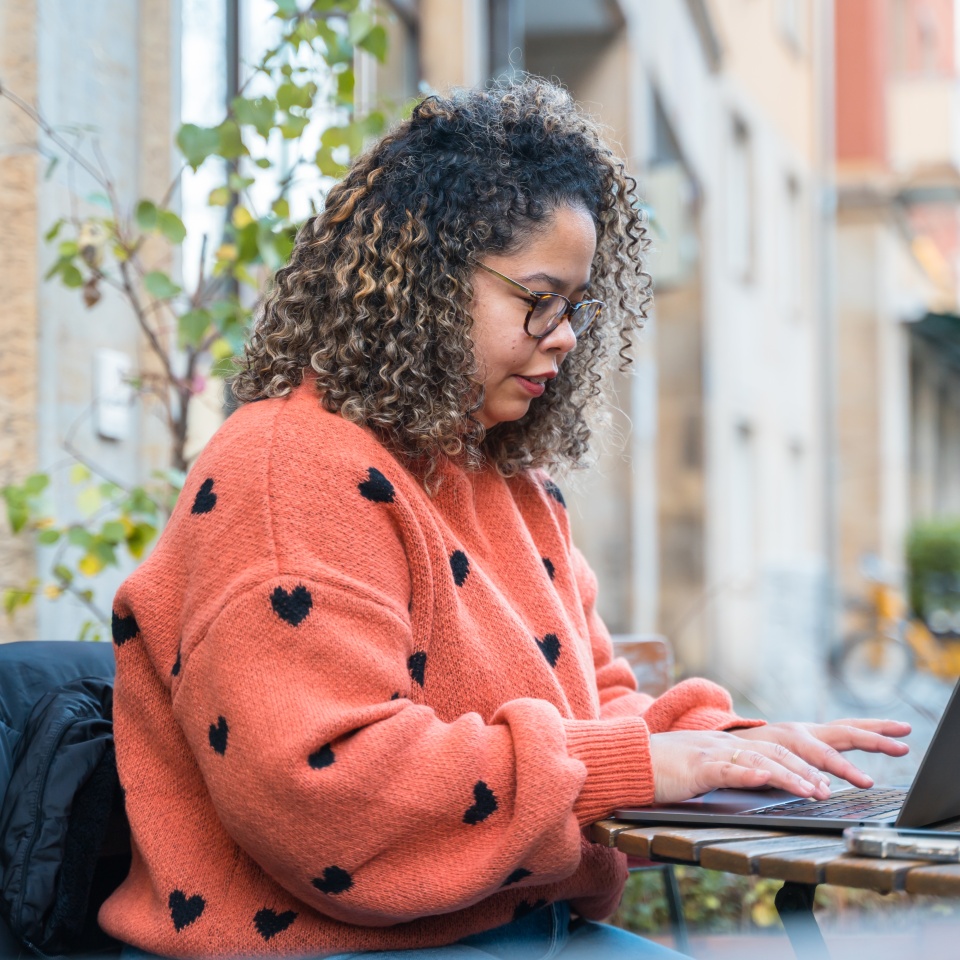 Woman typing on laptop at an outdoor european cafe, enjoying remote work