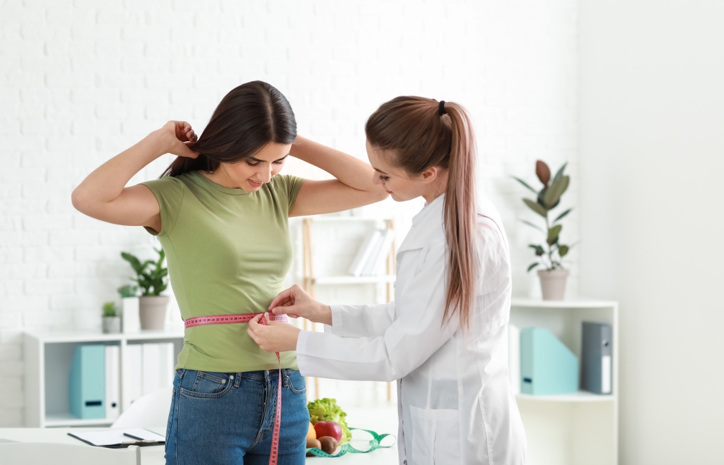 Nutritionist measuring waist of young woman in weight loss clinic